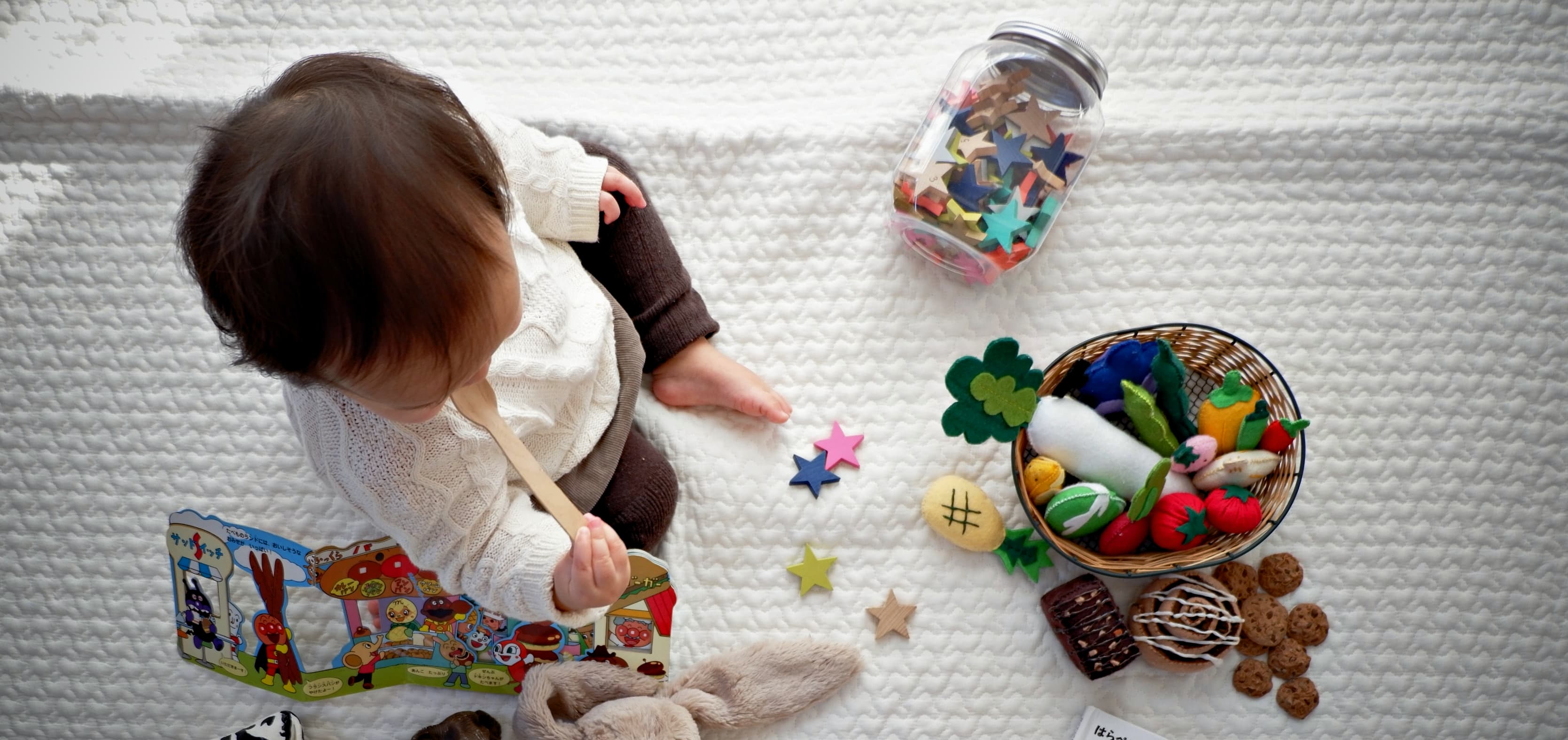 En litet barn sitter bland leksaker på en filt.